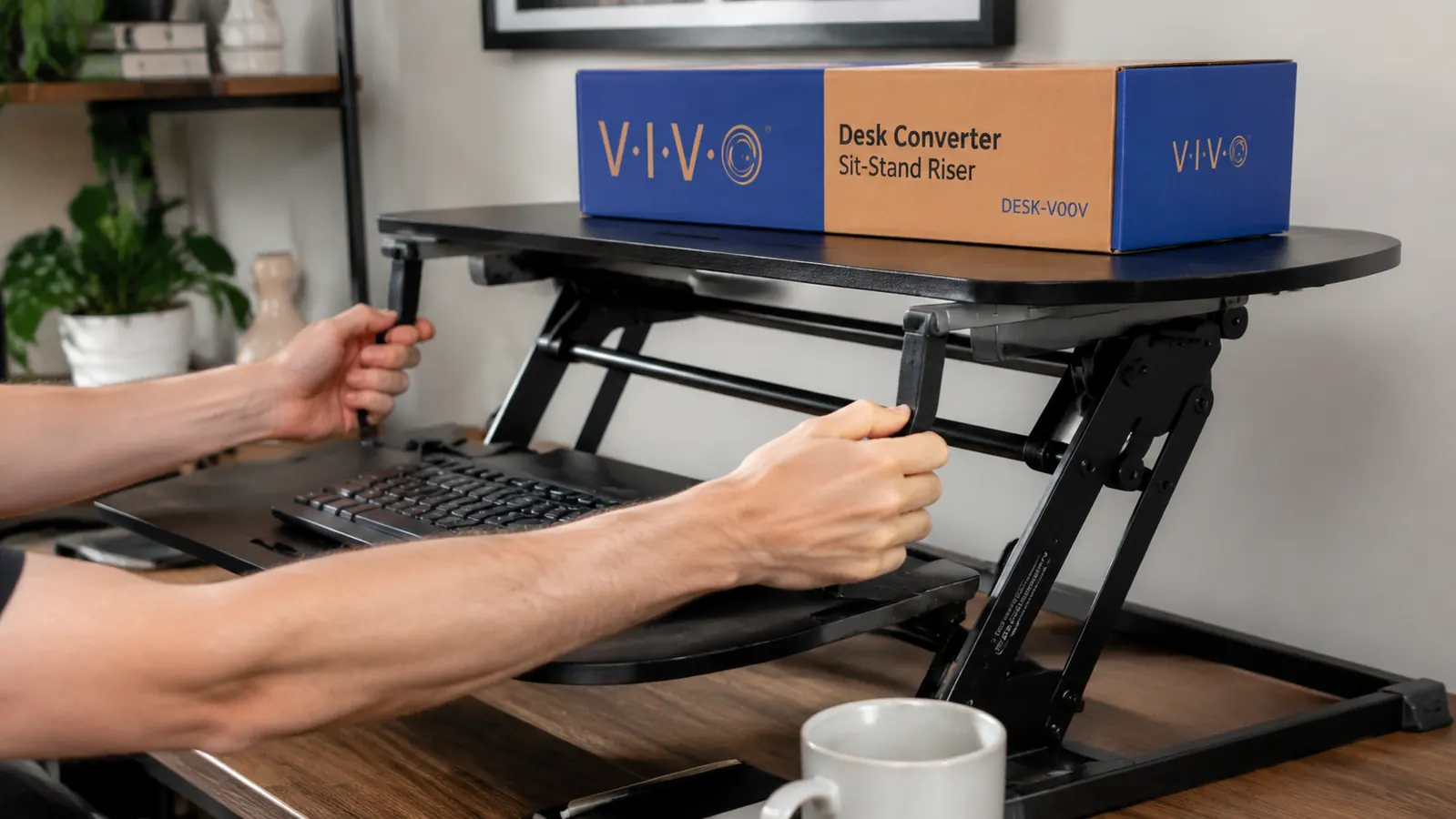 Close-up of hands adjusting the height-lift handle on a VIVO desk converter beside a keyboard and coffee mug