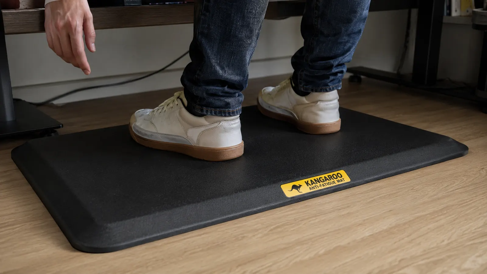 Close-up of feet standing on a thick black anti-fatigue mat in front of a desk