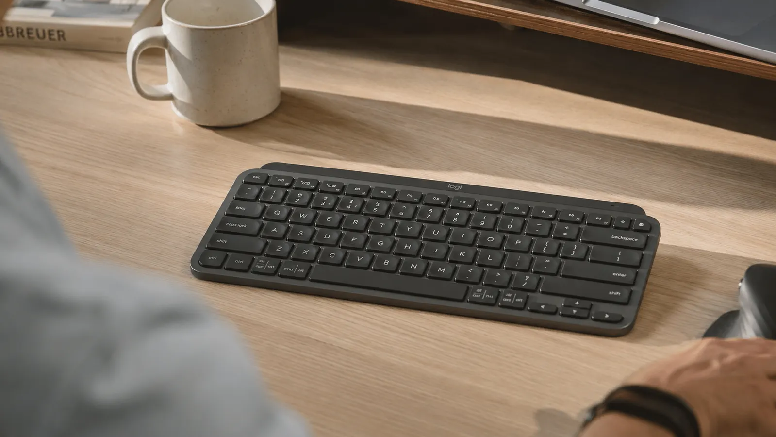 Logitech MX Keys Mini compact keyboard on a clean home office desk next to a coffee mug and monitor