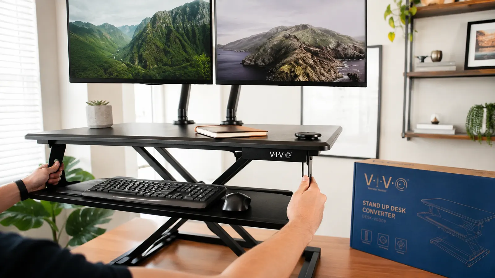 Person raising the VIVO K-Series 32-inch desk converter to standing height with a laptop and external monitor on the platform